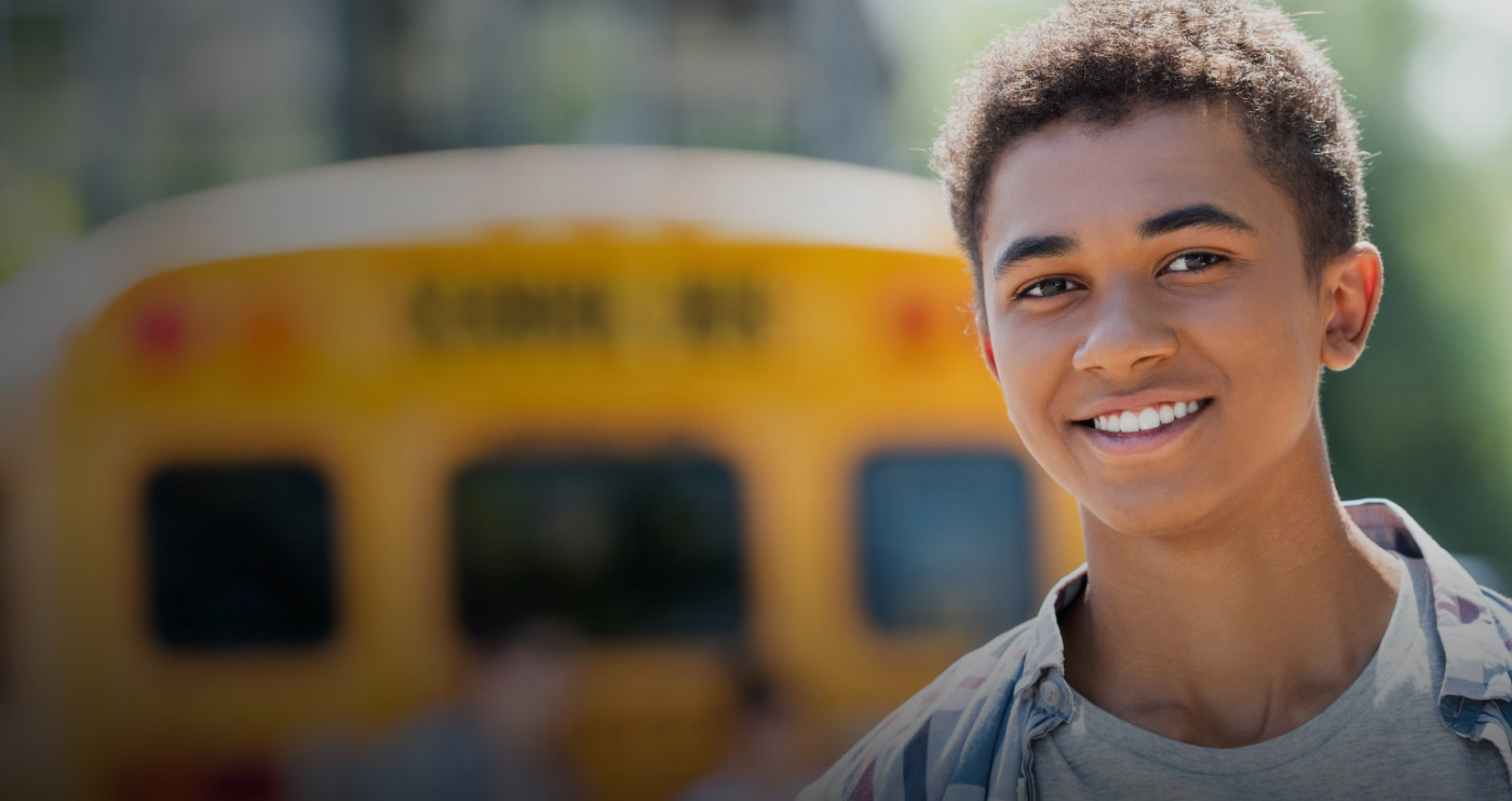 Teenage boy smiling with school bus in background