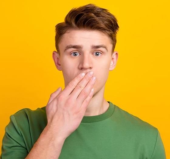 Teen boy covering his mouth, standing against yellow background