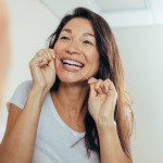 Woman smiling while flossing her teeth in bathroom