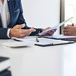 Two men sitting at desk, discussing paperwork