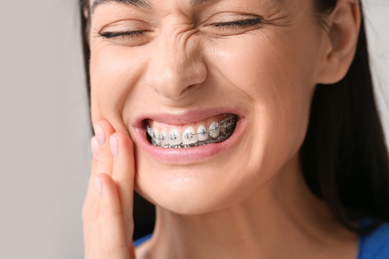 A grimacing woman with braces suffering mouth pain